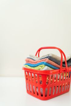 Multi-colored towels lie in a red laundry basket on a white background. Laundry and ironing