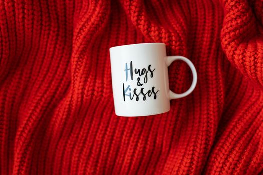 Hugs and kisses inscription on a white cup on a red knitted fabric. Love concept. St. Valentine's Day