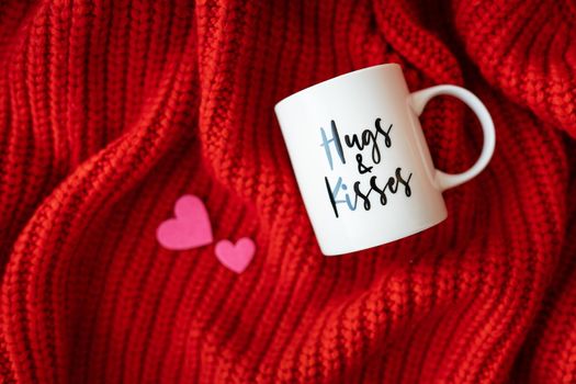 Hugs and kisses inscription on a white cup on a red knitted fabric. Love concept. St. Valentine's Day