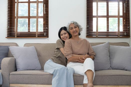 Portrait of Asian lovely family, young daughter hugging older mother. Attractive woman and senior elder mature mom sit on sofa, enjoy activity at home together in living room