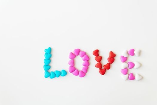 Valentine's day pattern background flat lay top view of bright candies in the shape of the word love scattered on a white background