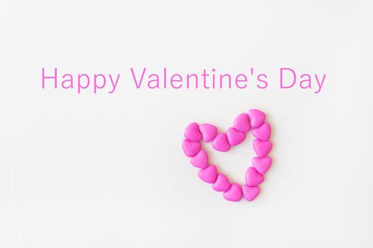 Valentine's day pattern background flat lay top view of heart shaped pink candies scattered on white background. Inscription happy valentine's day