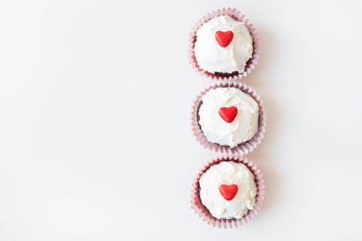 Valentine-14 February. Sweet chocolate muffins with butter cream and a red heart for decoration on a white background