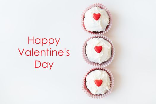 Valentine-14 February. Sweet chocolate muffins with butter cream and a red heart for decoration on a white background. Happy valentines day lettering