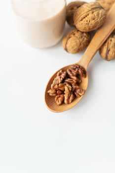 Vegan milk from nuts in a glass cup with various nuts on a white table, nuts in a wooden spoon