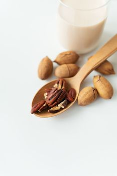 Vegan pecan milk in a glass cup with whole nuts on a white table, nuts in a wooden spoon