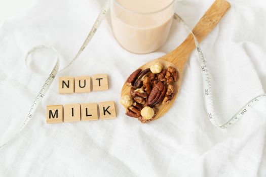 Vegan milk from nuts in a glass cup with various nuts on a white table, nuts in a wooden spoon. Lettering nut milk