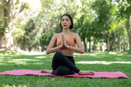 Yoga woman meditation praying outside in city park wellness. Summer exercise lifestyle active young Asian girl meditating background