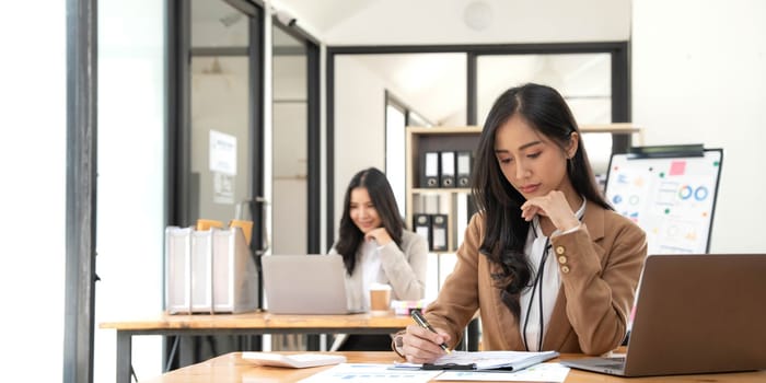 Asian Business woman using calculator and laptop for doing math finance on an office desk, tax, report, accounting, statistics, and analytical research concept.