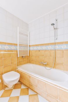 a bathroom with orange and white tiles on the walls, tub, toilet, and bathtub in one corner