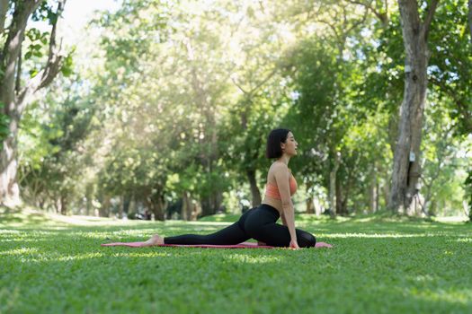 Young attractive girl is doing advanced yoga asana on the fitness mat in the middle of a park