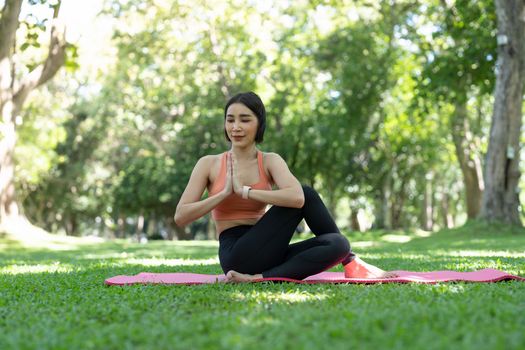 Young attractive girl is doing advanced yoga asana on the fitness mat in the middle of a park