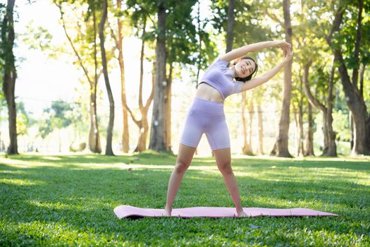 Attractive young Asian woman practice yoga, exercise in the park, standing one leg on a yoga mat, showing balance posture. Wellbeing lifestyle and activity concept.