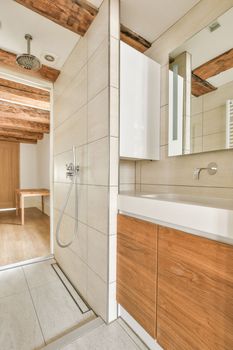 Shower faucets attached to tiled wall near glass partition and ornamental curtail in washroom at home