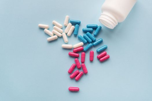 Various multicolored pills - blue, pink, white flying from an open plastic bottle, isolated on a light blue background