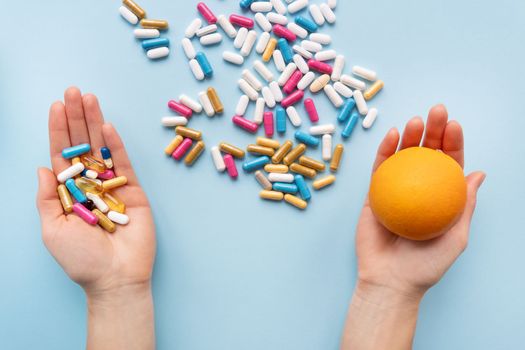 Many multi-colored pills, man's hands in one vitamins in another fresh orange. Health and treatment alternatives concept