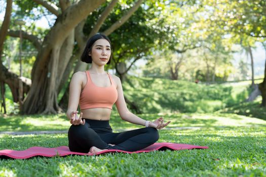 Yoga at park. Young asian woman in lotus pose sitting on green grass. Concept of calm and meditation