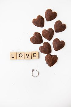 Truffle chocolate candies in the form of a heart on a white background. Inscription love made of wooden letters and a ring with a diamond. Hand and serge proposals, valentine