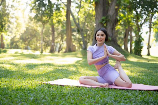 Attractive young Asian woman practice yoga, exercise in the park, standing one leg on a yoga mat, showing balance posture. Wellbeing lifestyle and activity concept.