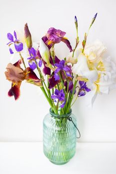 Crystal green vase full of faceted multi-colored hybrid bearded irises, vertical with copy space