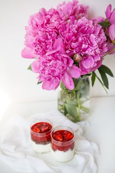 A beautiful bouquet of pink peonies in a vase on a white table stands along with a heart-shaped strawberry dessert. St. Valentine's Day, 8 March