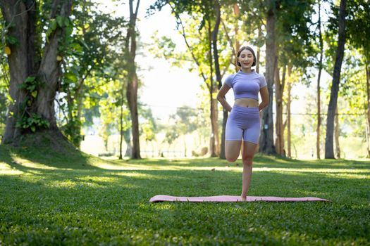 Attractive young Asian woman practice yoga, exercise in the park, standing one leg on a yoga mat, showing balance posture. Wellbeing lifestyle and activity concept.