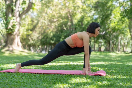 Young attractive girl is doing advanced yoga asana on the fitness mat in the middle of a park