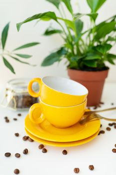 Beautiful morning, the process of making coffee. An automatic drip coffee maker stands with a yellow cup on a white table, scattered coffee beans. Green flowerpot on the background