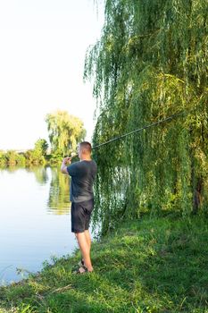 Fishing Reel. The guy throws a fishing rod against the backdrop of the lake. The concept of relaxation and hobby for the soul