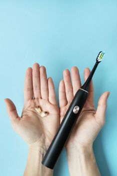 A modern electric toothbrush in one hand and pulled teeth in the other hand on a blue background. Tooth extraction operation. The concept of hygiene for daily care of the oral cavity in order not to lose a tooth