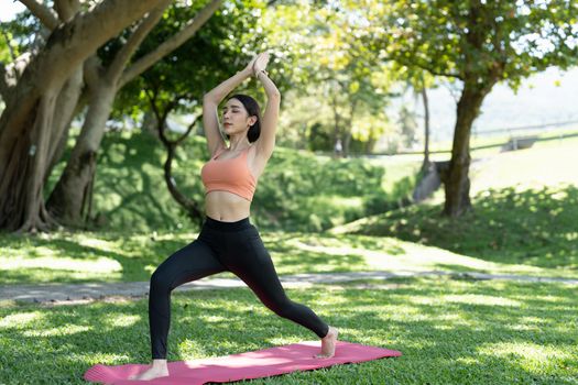 Young attractive girl is doing advanced yoga asana on the fitness mat in the middle of a park