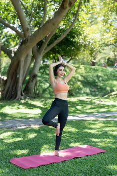 Young attractive girl is doing advanced yoga asana on the fitness mat in the middle of a park