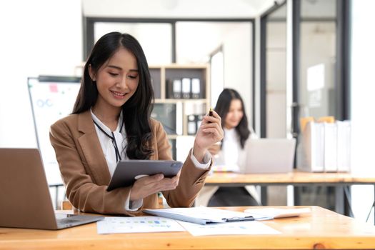 Asian Business woman using calculator and laptop for doing math finance on an office desk, tax, report, accounting, statistics, and analytical research concept.