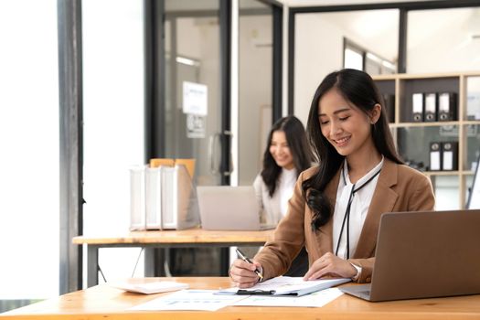 Asian Business woman using calculator and laptop for doing math finance on an office desk, tax, report, accounting, statistics, and analytical research concept.