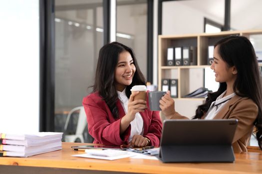 Two young Asian businesswomen show joyful expression of success at work smiling happily with a laptop computer in a modern office..