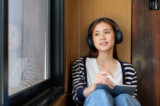 Young attractive asian female with headphone listening music on digital tablet