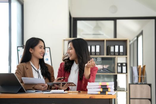 Two young Asian business woman talk, consult, discuss working with new startup project idea presentation analyze plan marketing and investment in the office..