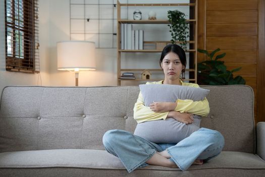 Hand on temples of young unhappy sadness Asian girl sitting on sofa. She is feeling not very good due to her sickness and having a headache. Seen from the front. Stress and sickness concept...