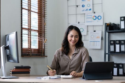 Asian woman accountant preparing annual financial report checking result on calculator bookkeeping. female freelancer counting tax rates declaring income.