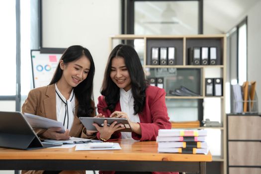 Two young Asian business woman talk, consult, discuss working with new startup project idea presentation analyze plan marketing and investment in the office..