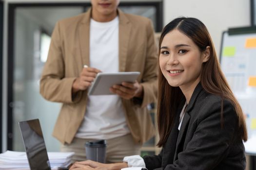 Beautiful smiling Asian woman working at the office, looking at the camera