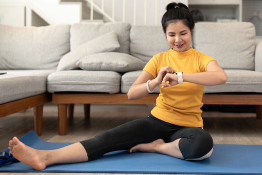 Attractive young woman using smartwatch during yoga stretching yoga online at home. Self-isolation is beneficial, entertainment and education on the Internet. Healthy lifestyle concept.