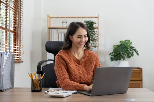 Beautiful young smiling Asian businesswoman working on laptop and drinking coffee, Asia businesswoman working document finance and calculator in her office