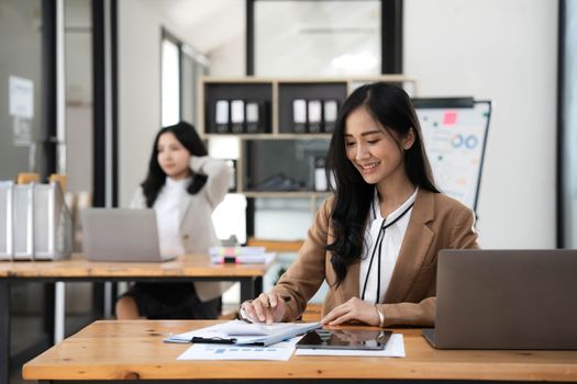 Two young Asian business woman talk, consult, discuss working with new startup project idea presentation analyze plan marketing and investment in the office...