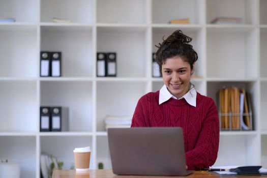 Photo of cheerful young woman working using computer laptop concentrated and smiling at office..