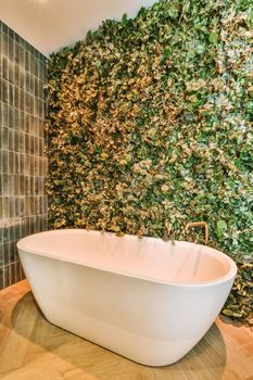 a bathtub in front of a green wall with plants on the walls and flooring it is surrounded by tiles