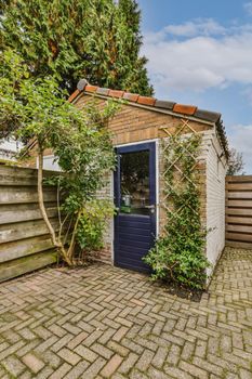 an outside area with a blue door and brick walls, surrounded by green trees on either side of the building