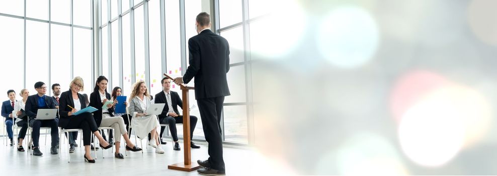 Group of business people meeting in a seminar conference widen view . Audience listening to instructor in employee education training session . Office worker community summit forum with speaker .