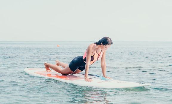 Woman sup yoga. Happy young sporty woman practising yoga pilates on paddle sup surfboard. Female stretching doing workout on sea water. Modern individual female outdoor summer sport activity