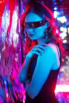 Close-up portrait of caucasian woman in sunglasses in neon light against foil wall